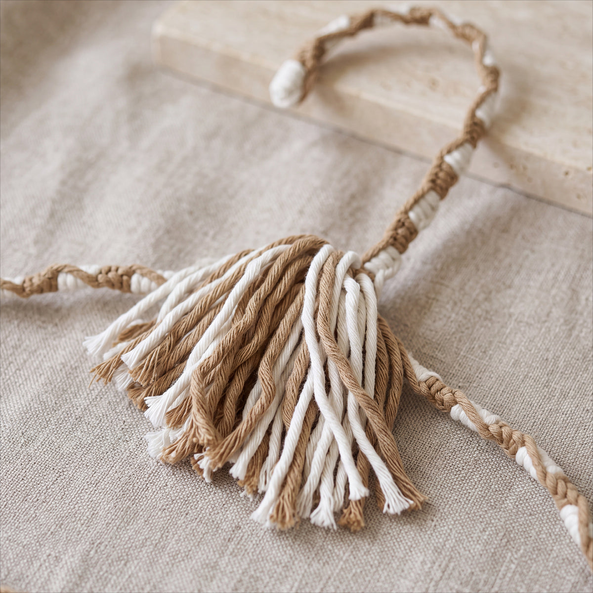 Natural Linen cream-and-sand hand-knotted cotton hanger displayed on textured linen